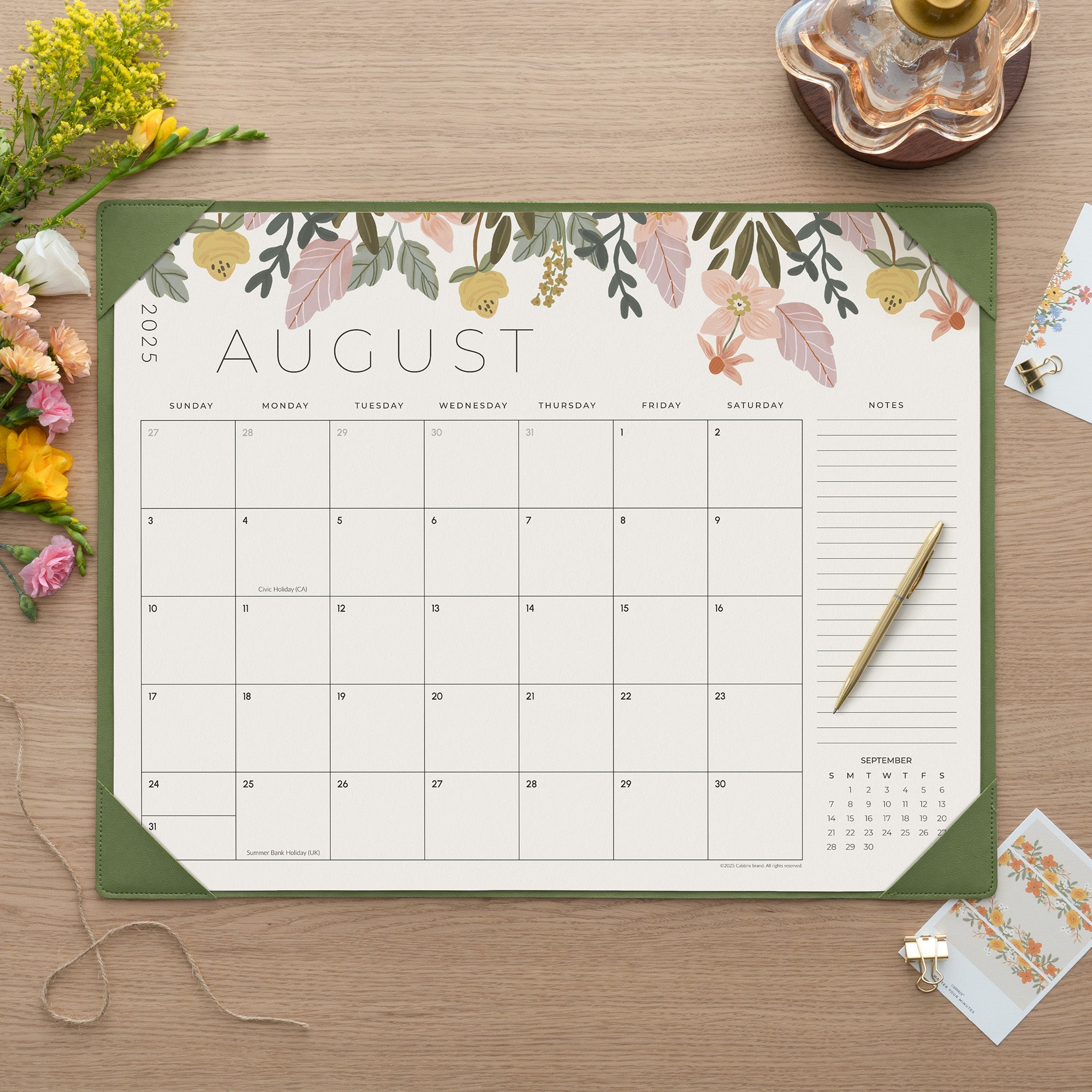 Floral August 2023 calendar on a wooden surface with flowers and a pen.