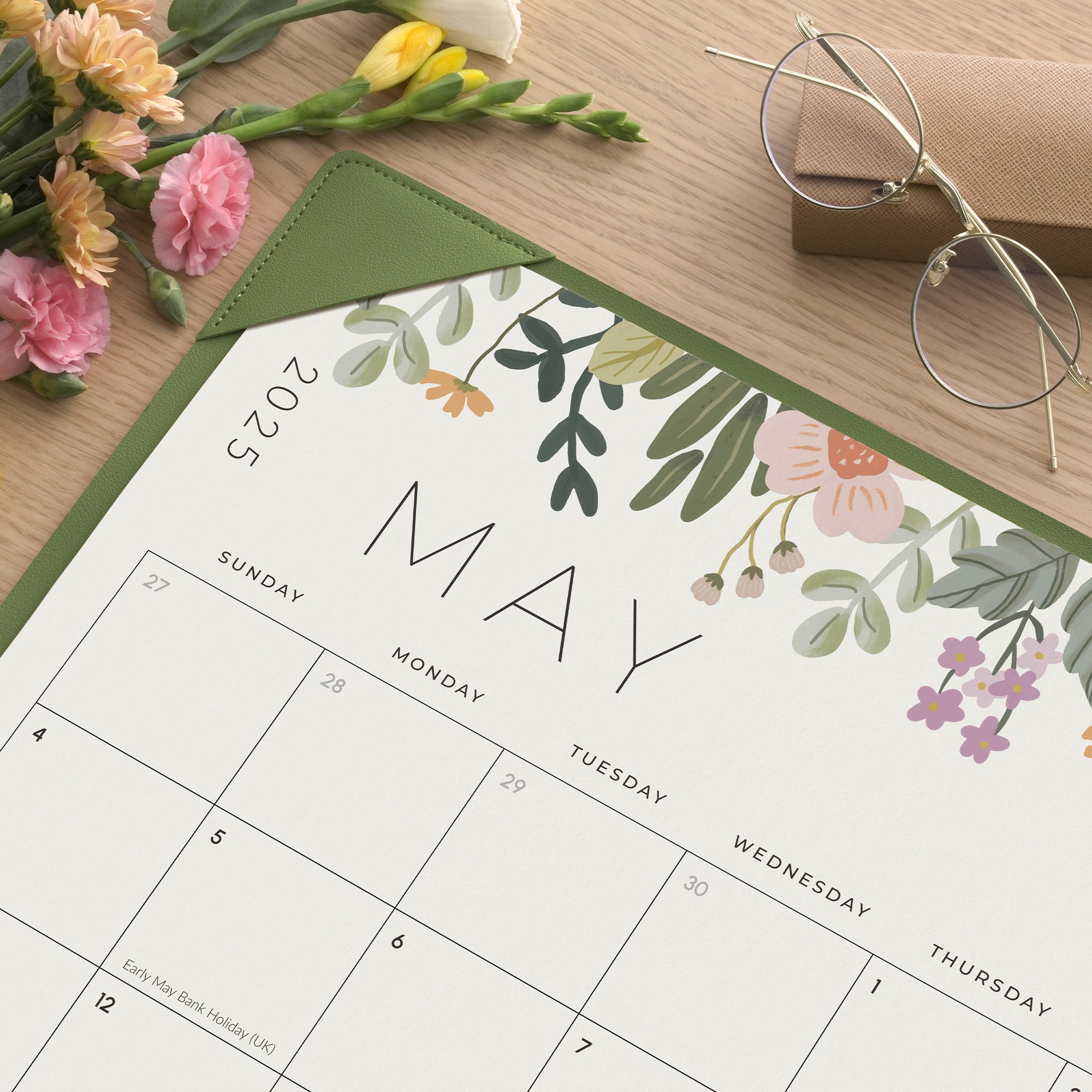 Floral-themed calendar for May 2025 on a wooden surface with flowers and glasses.