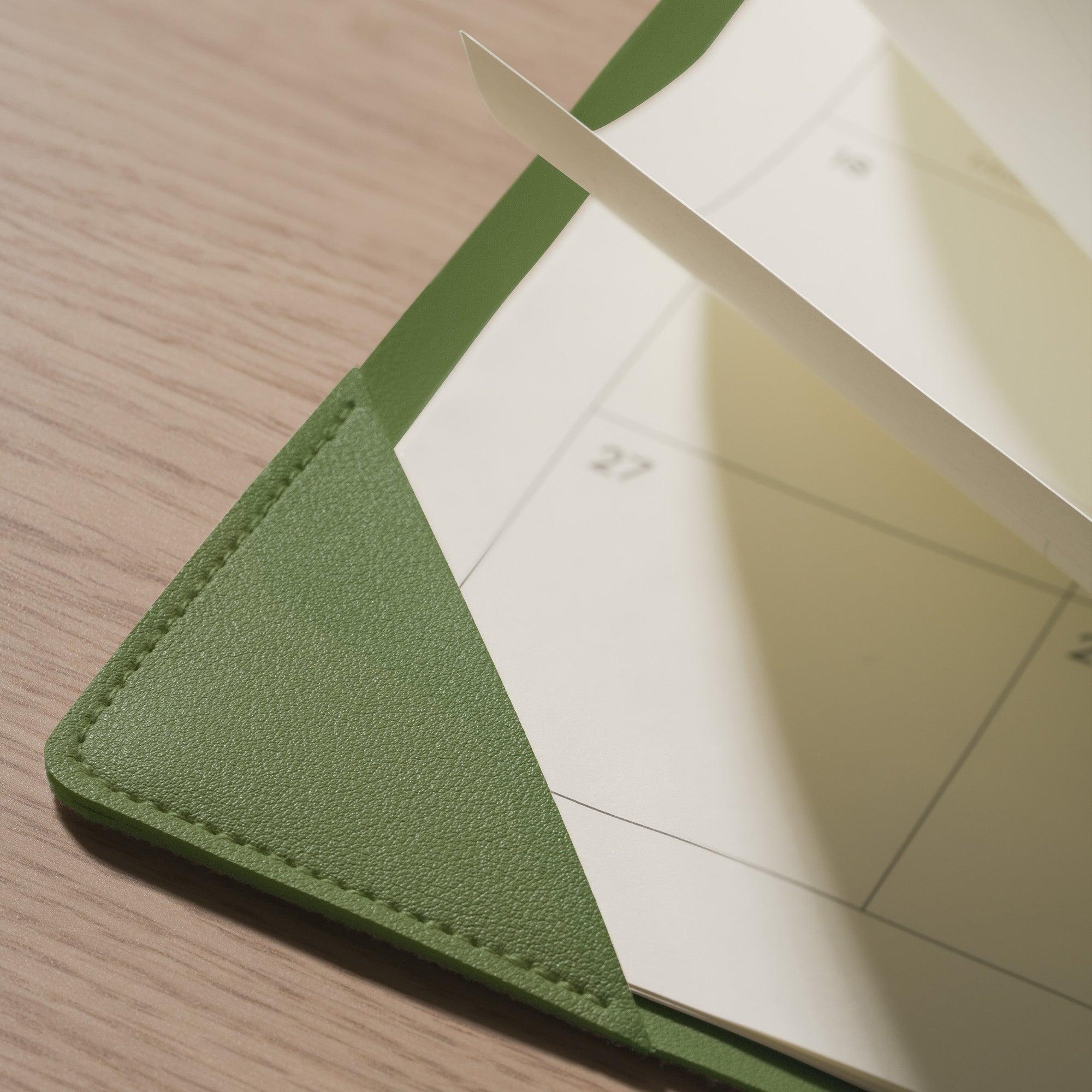 Green leather-bound notebook with a white page on a wooden surface