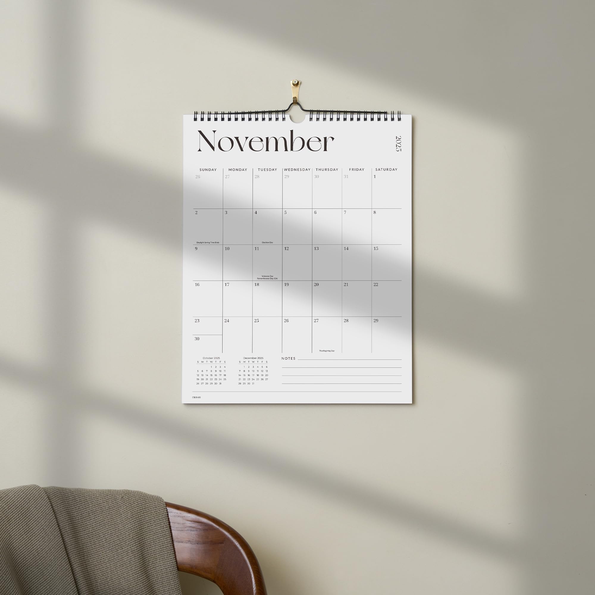 Wall calendar for November hanging on a light beige wall with a chair and blanket in the foreground.