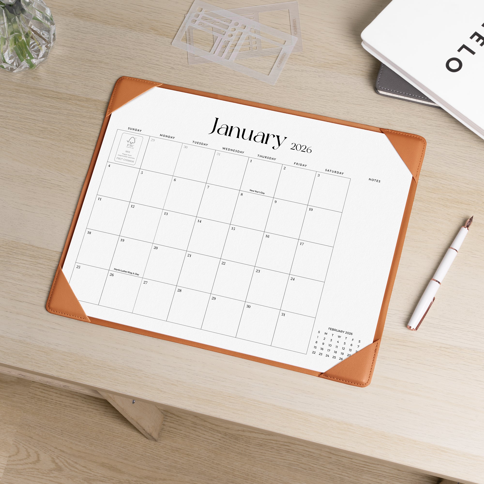 Calendar pad with January 2026 on a wooden desk with a pen and glass.