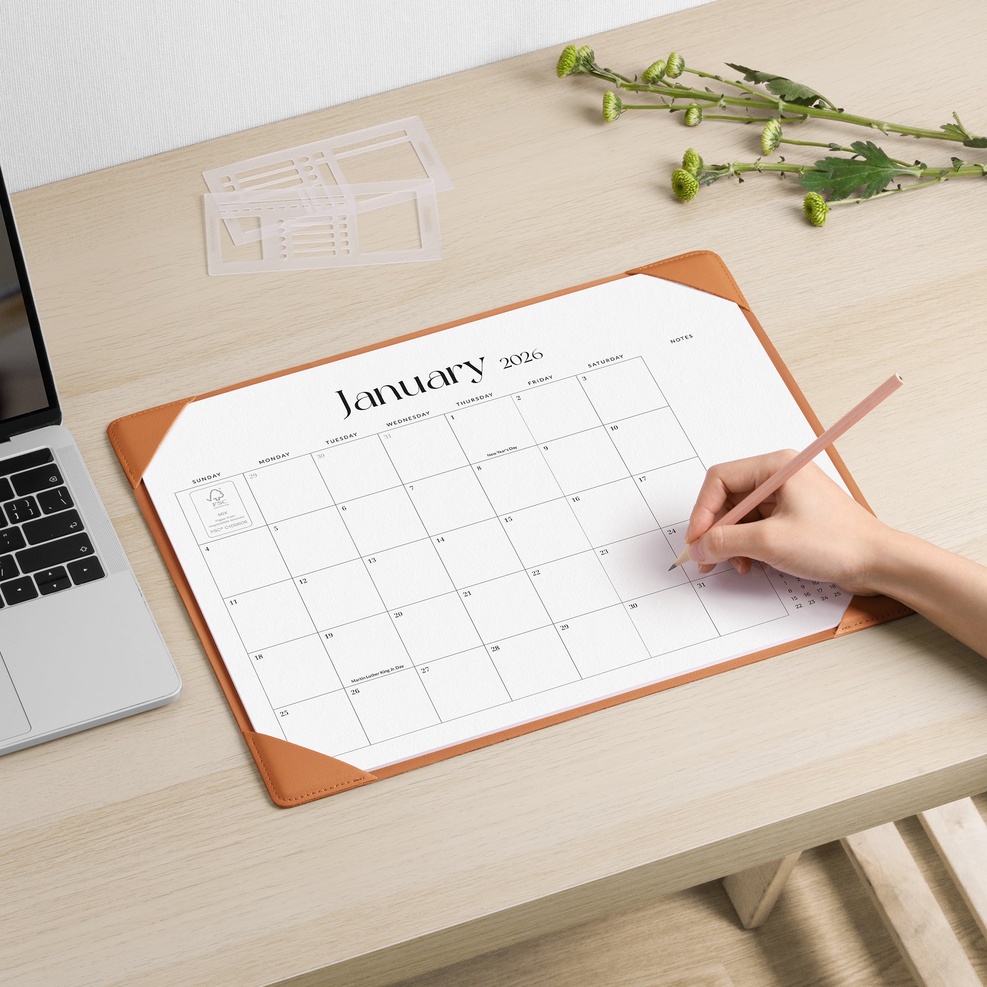 Person using a pen to mark on a January 2020 calendar on a desk with a laptop and decorative elements.