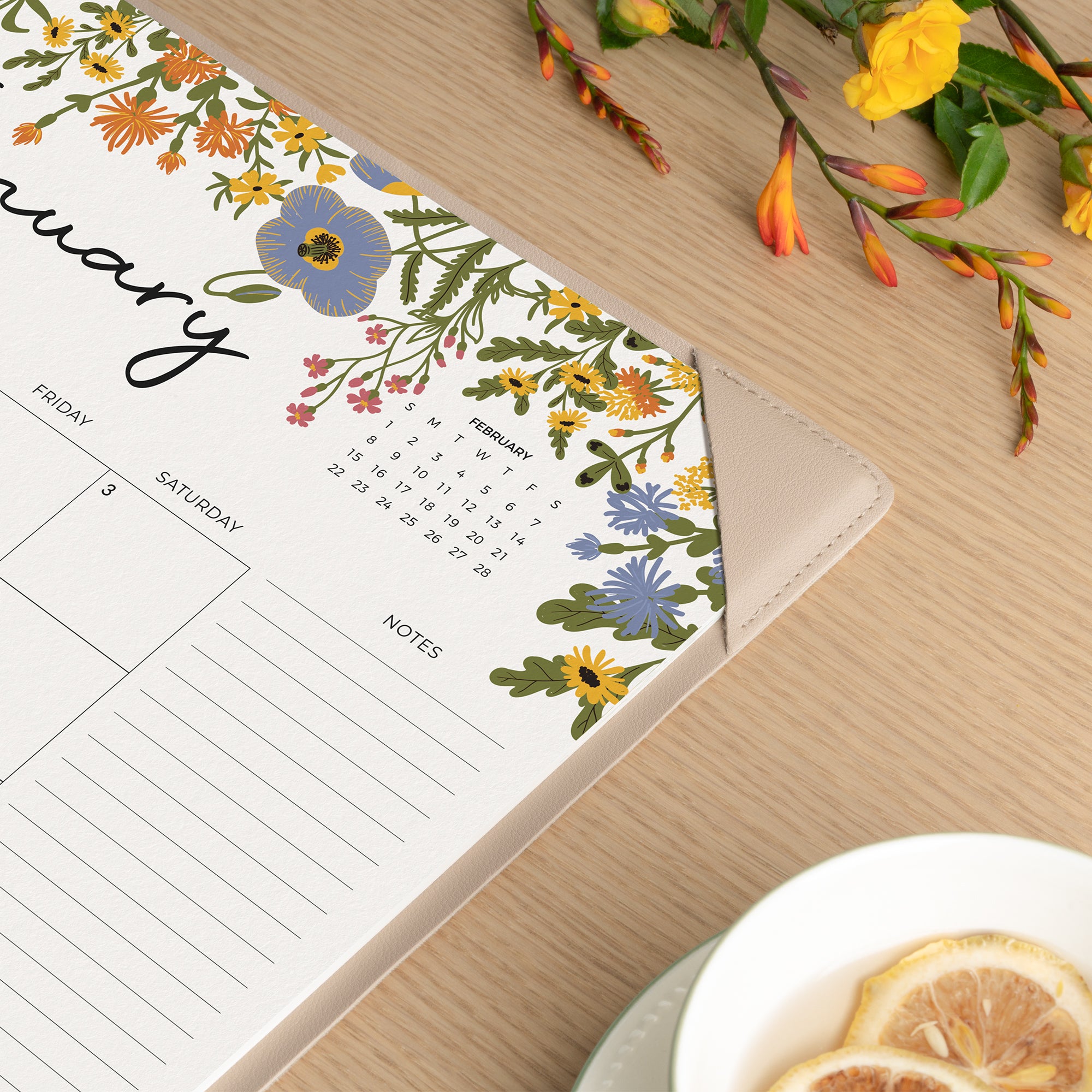 Floral-themed calendar on a wooden surface with flowers and a teacup.