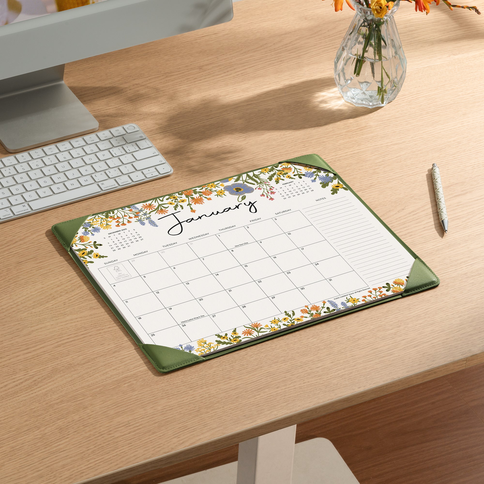 Floral calendar pad on a desk with a computer and flowers in the background