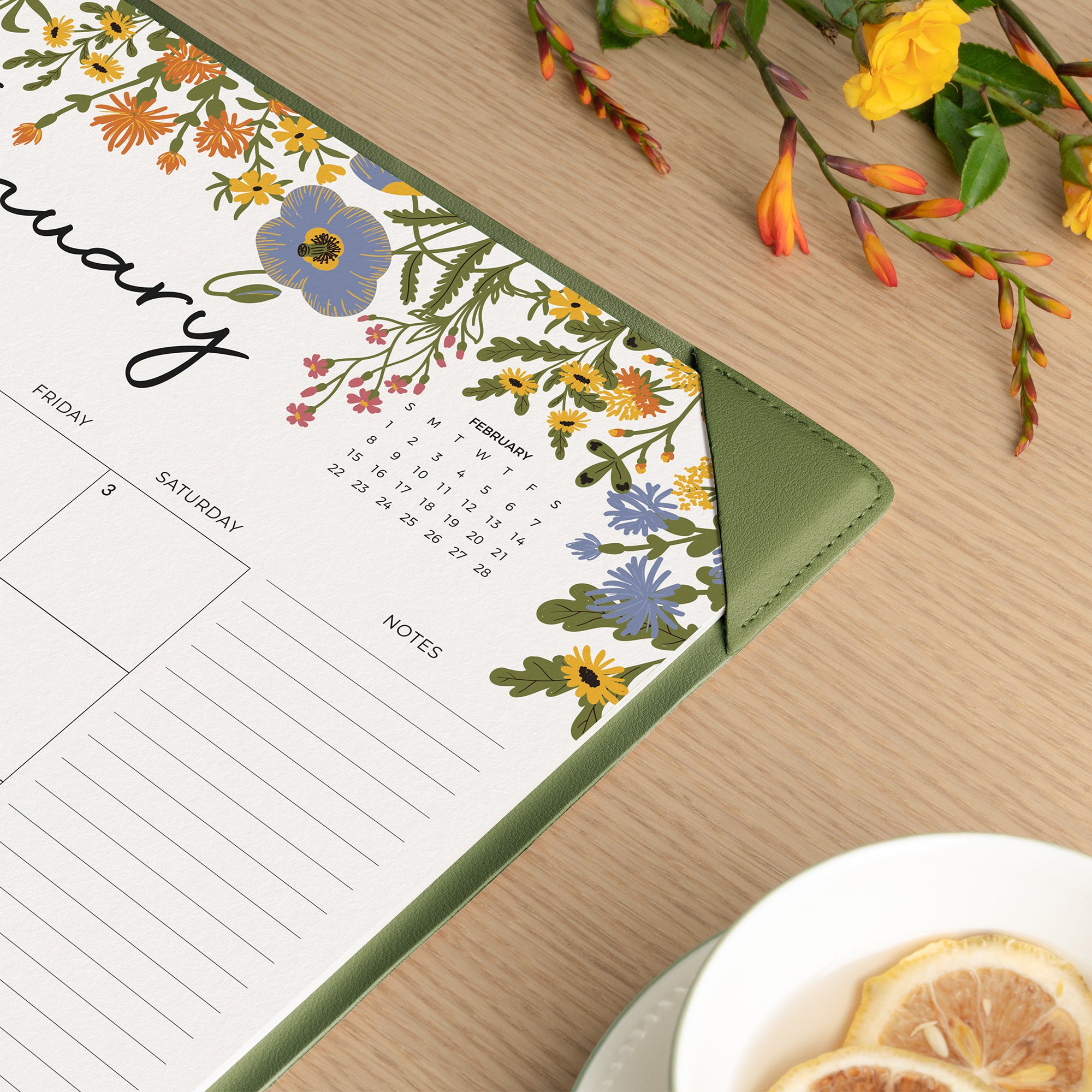 Floral-themed calendar on a wooden surface with flowers and a teacup in the background