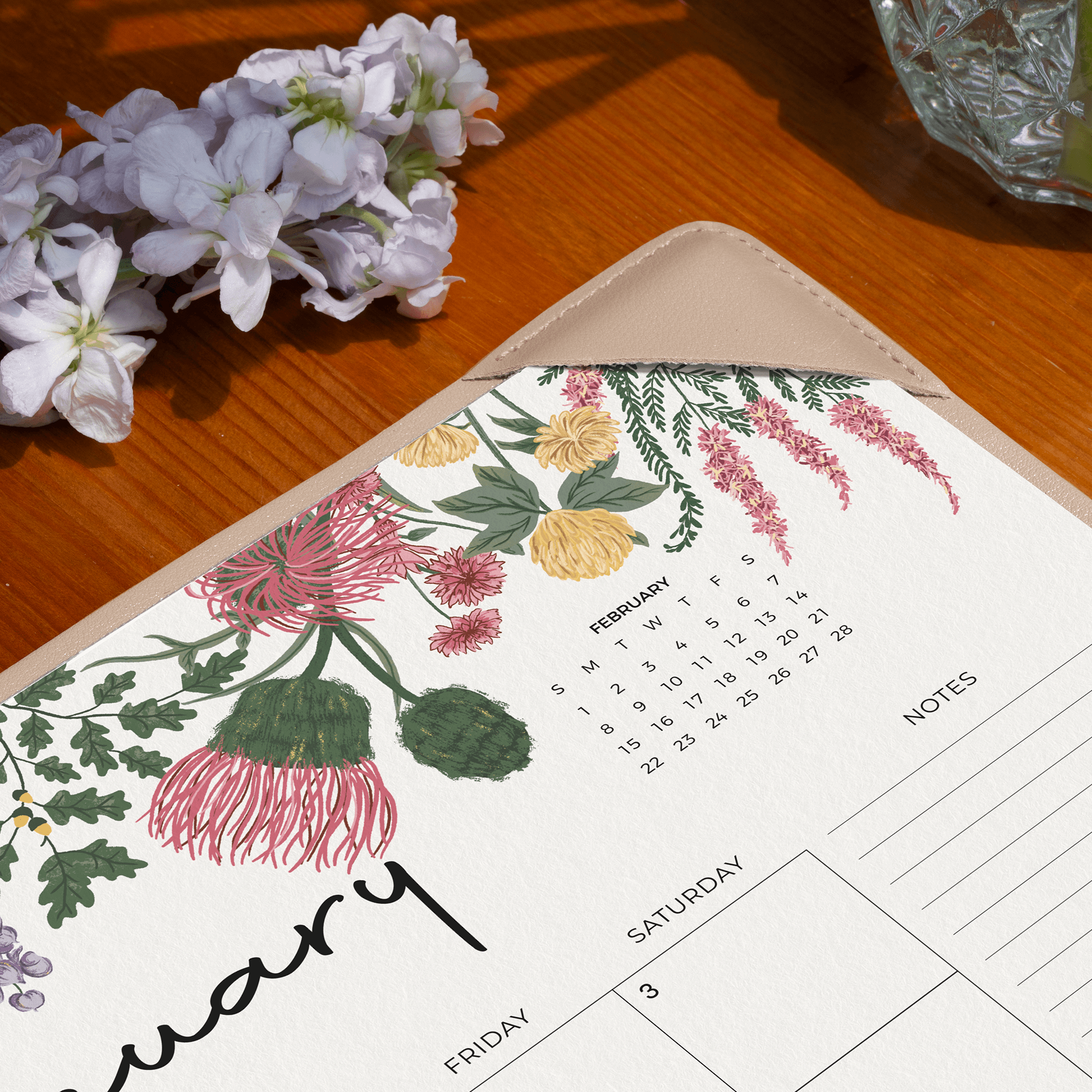 Floral-themed calendar postcard on a wooden surface with flowers and a glass container.