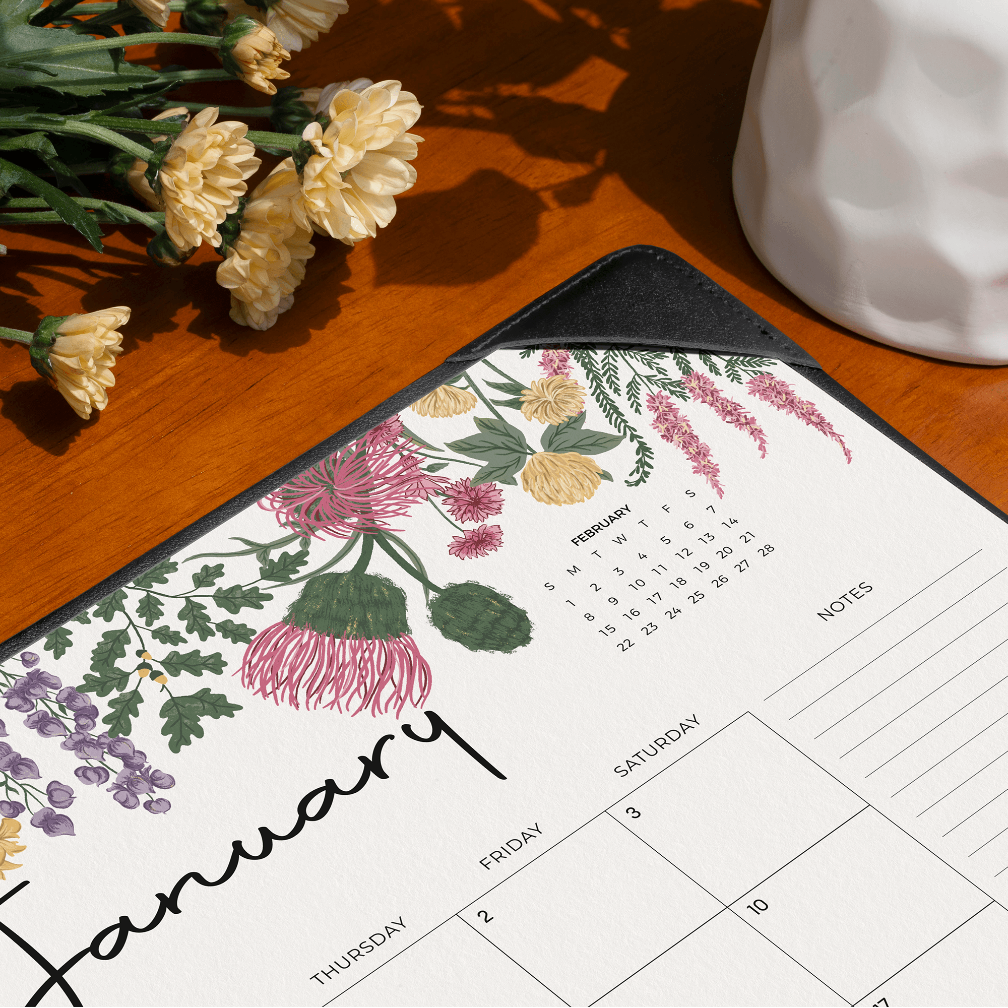 Floral-themed calendar on a wooden surface with flowers and a white vase.