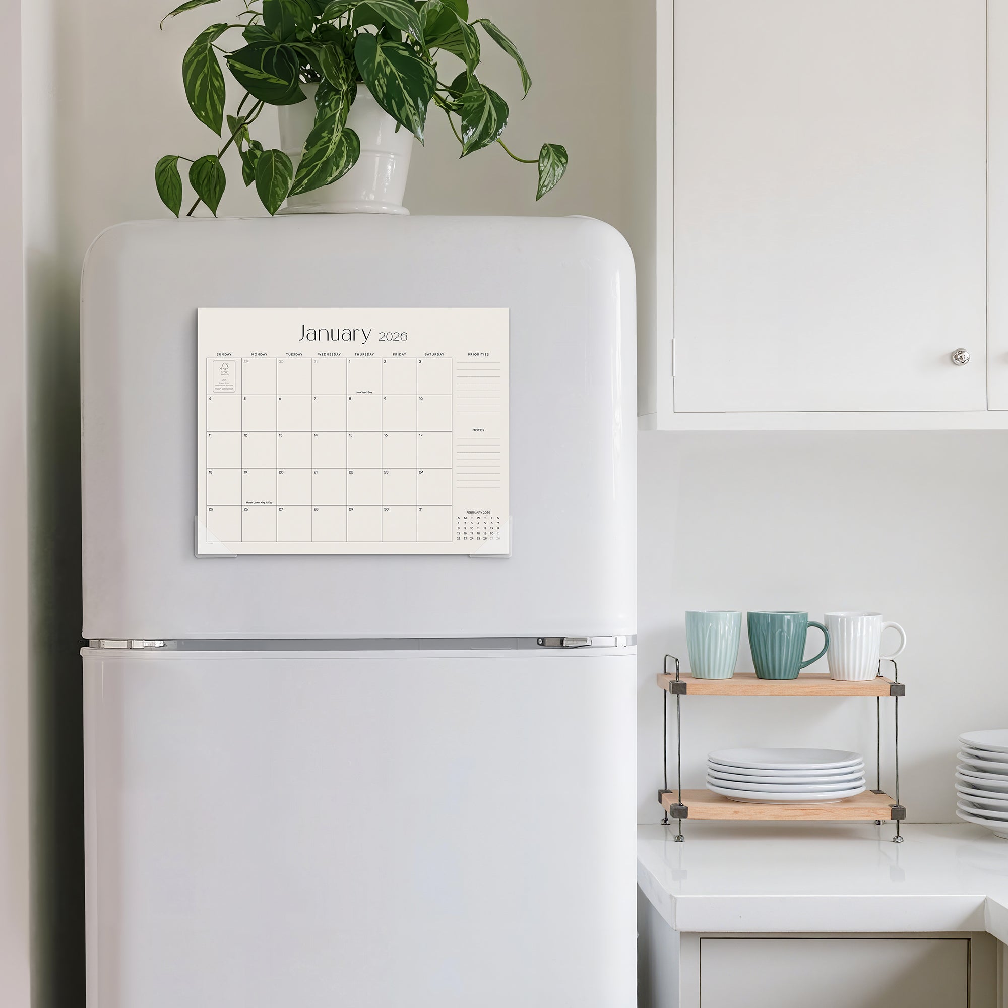 White refrigerator with a calendar on a kitchen counter with a plant and shelves.