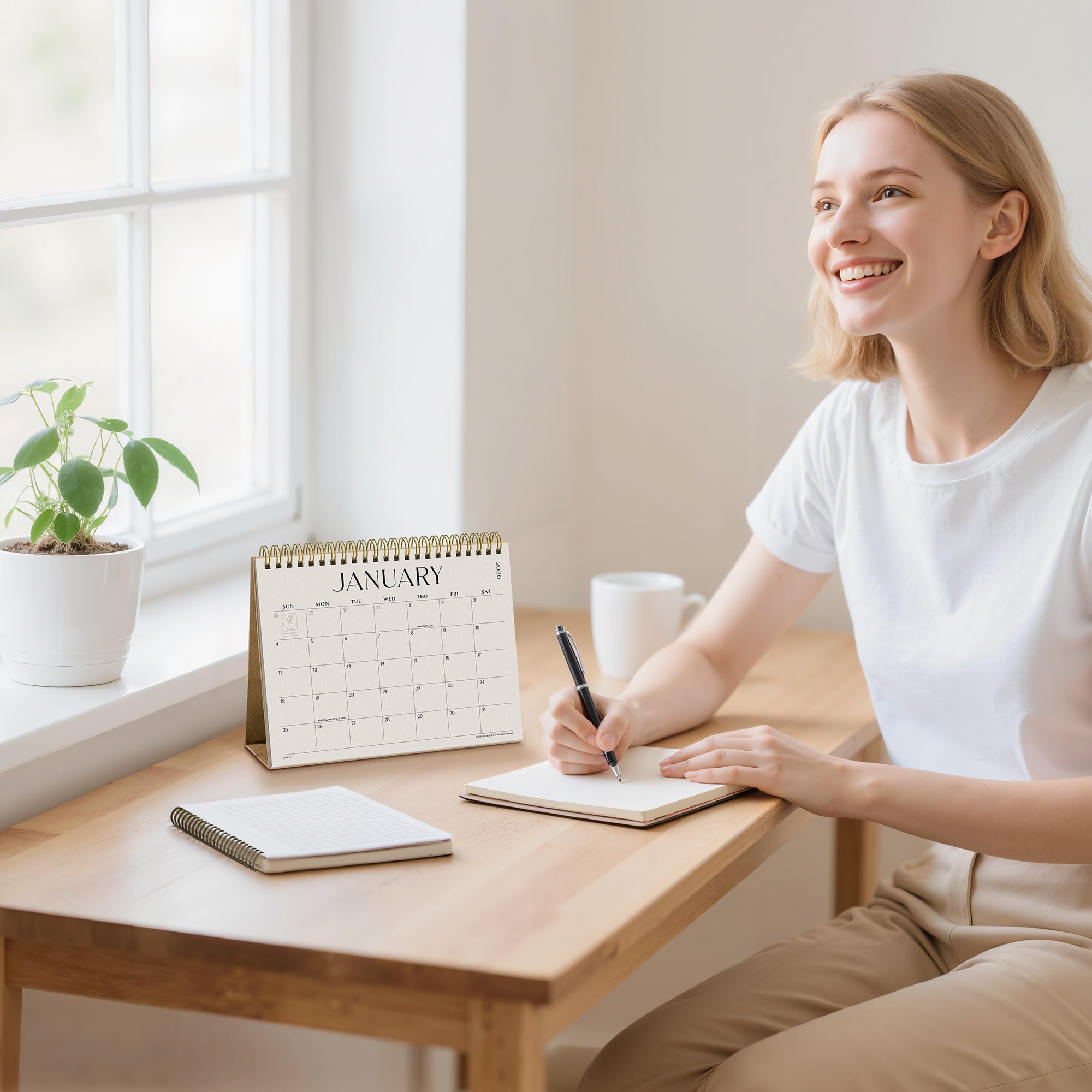 Woman sitting at a desk with a calendar, notebook, and pen, smiling.