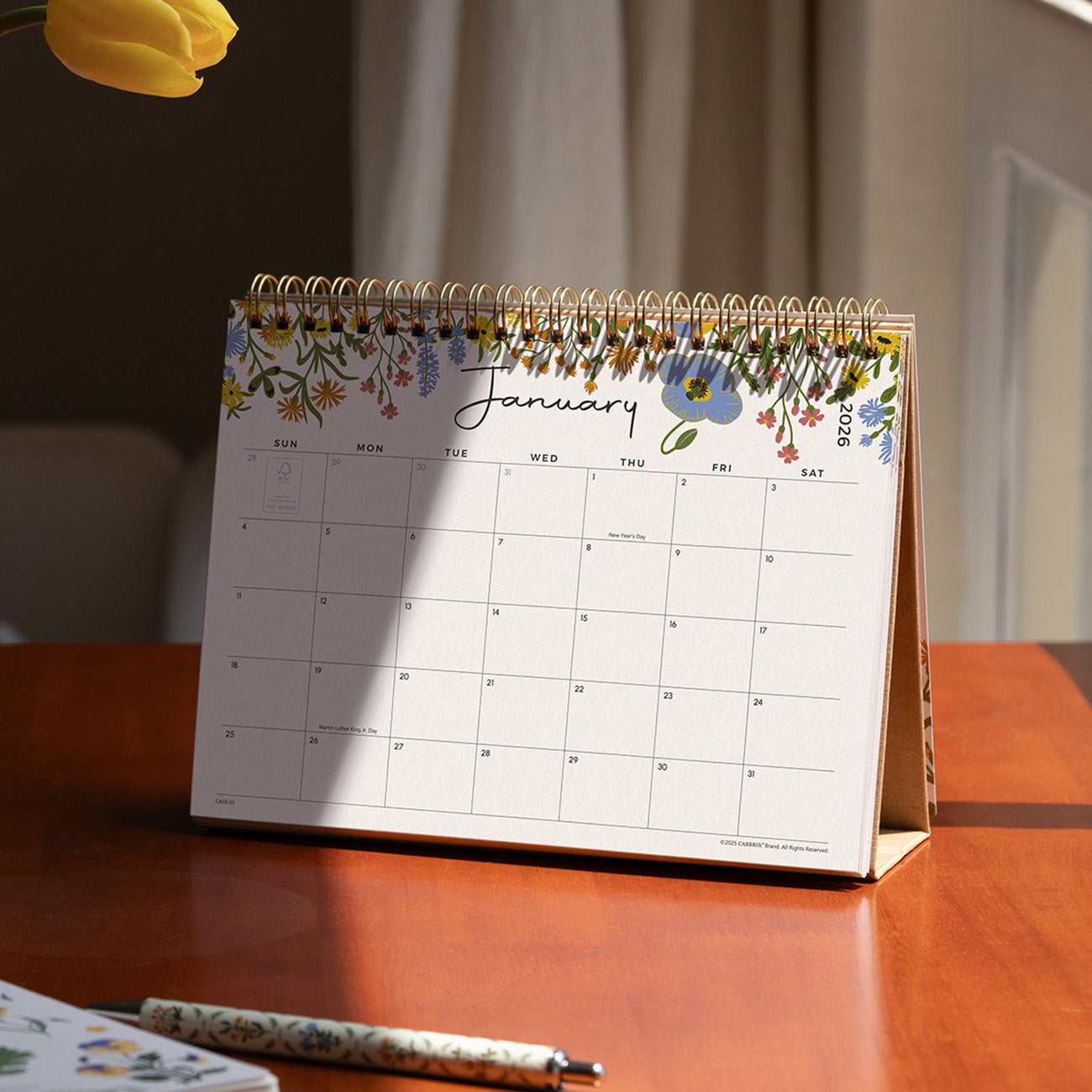 Floral desk calendar on a wooden surface with a pen and paper.