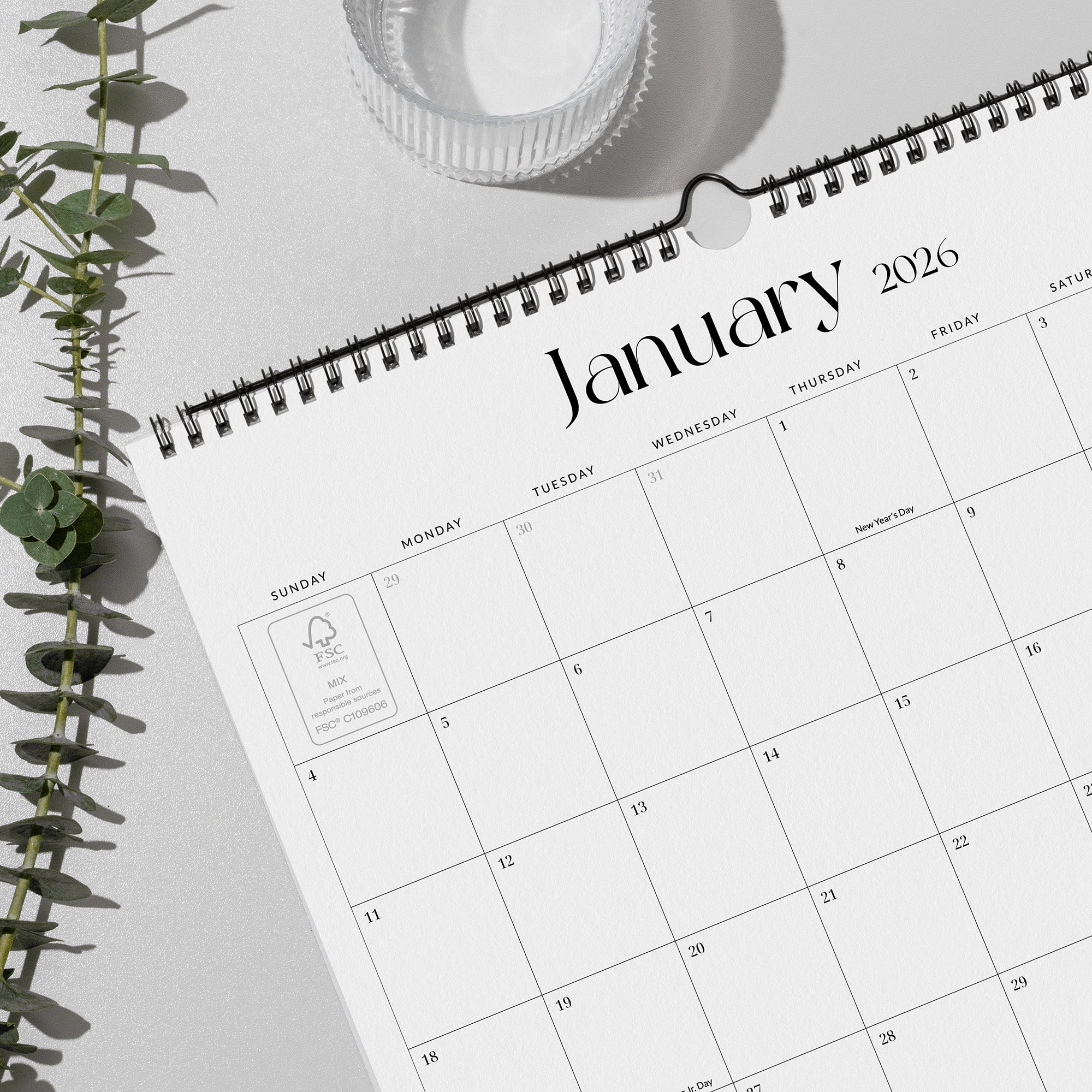 Calendar for January 2026 on a light surface with a plant and cup in the background