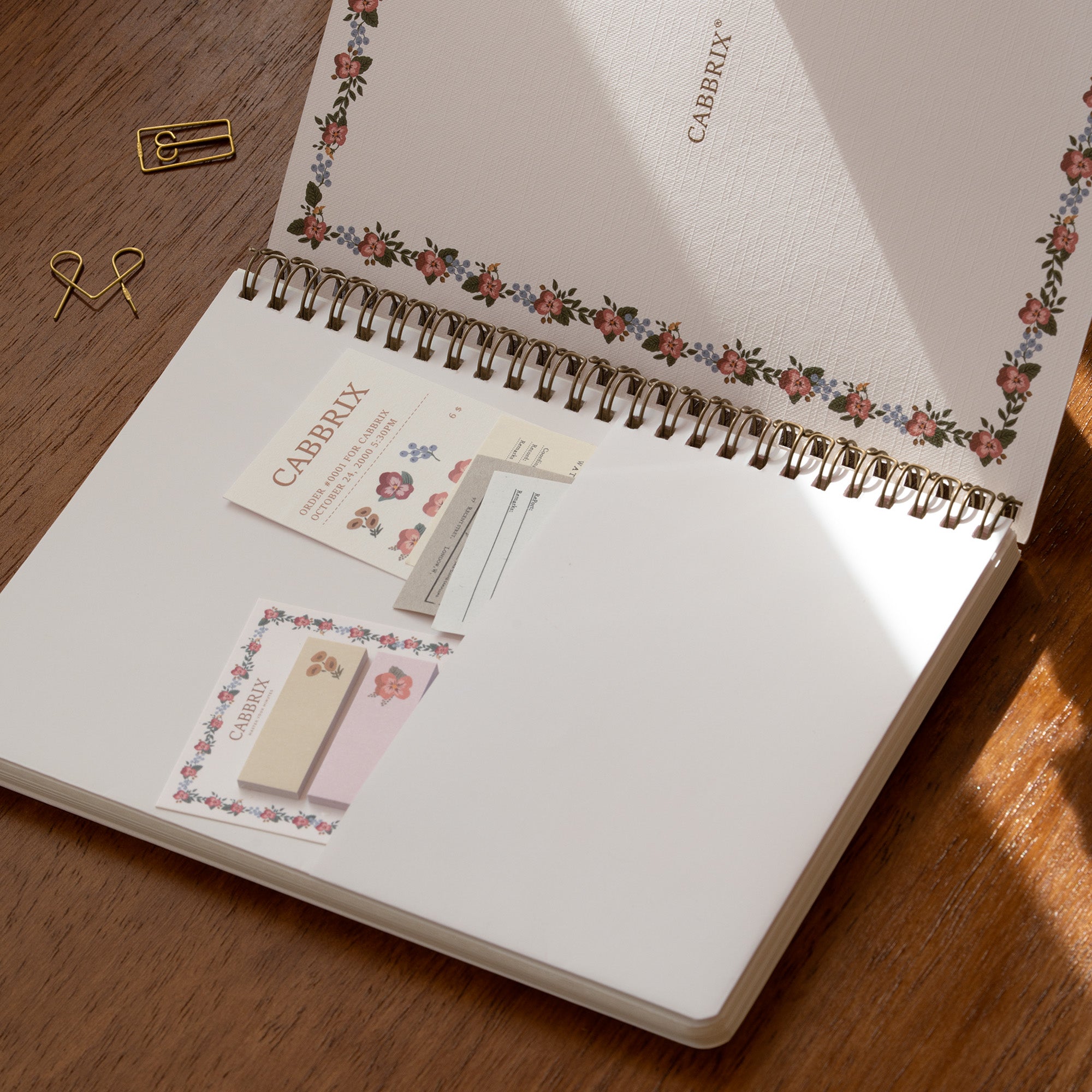 Open notebook with floral design on a wooden surface, featuring CABBIX products.