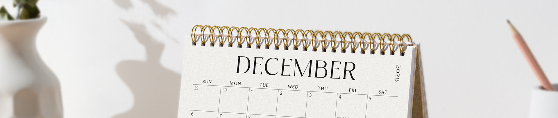 Calendar for December on a white surface with a pen and plant in the background