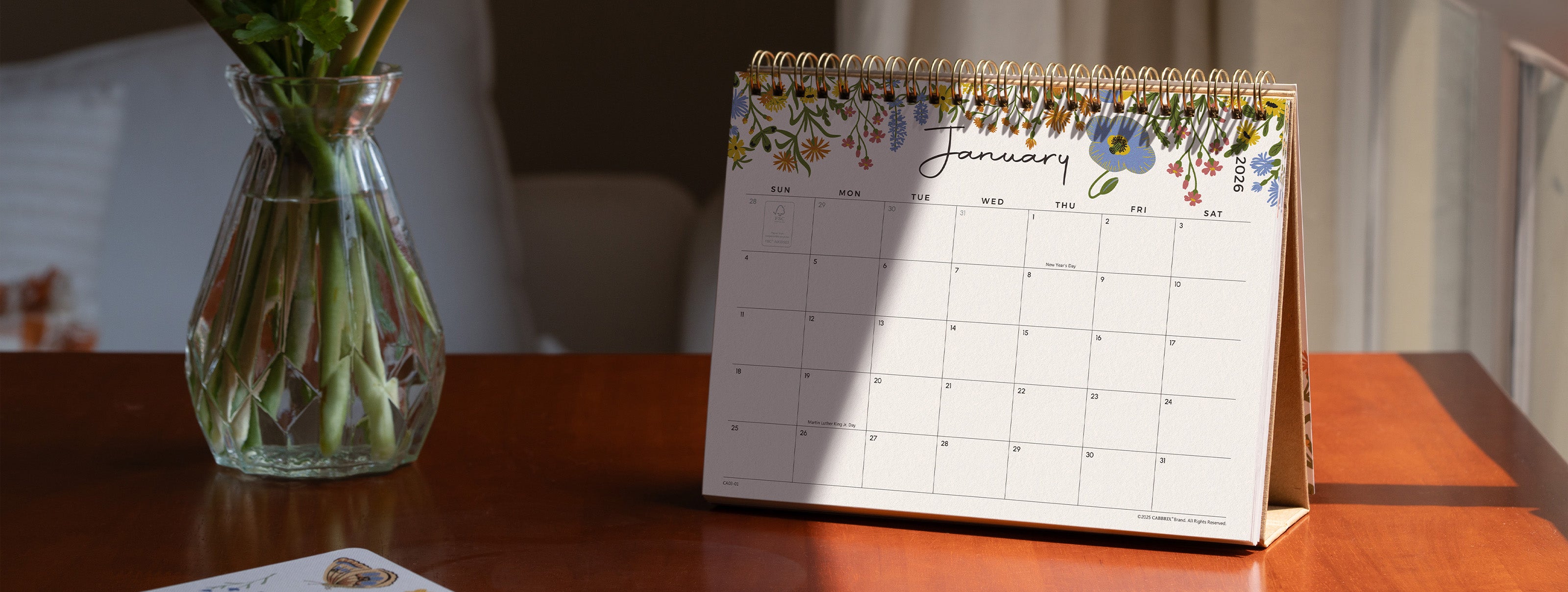Calendar on a wooden surface with a vase of flowers in the background