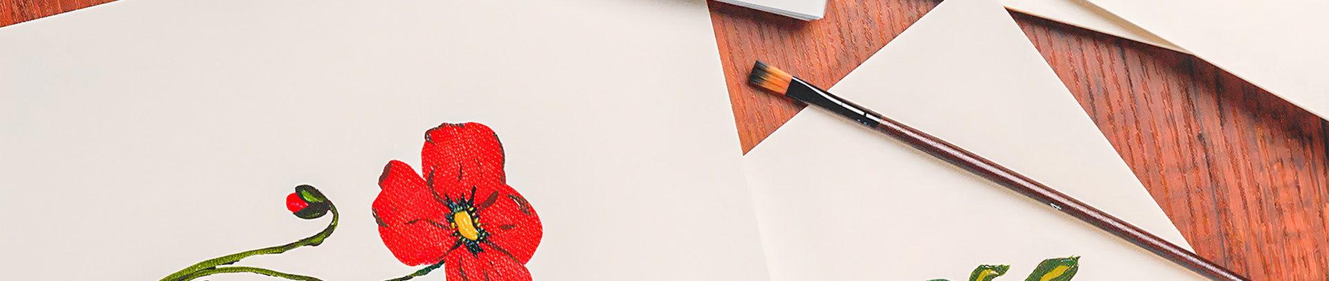 Red flower illustration on a white sheet of paper with a brush on a wooden surface