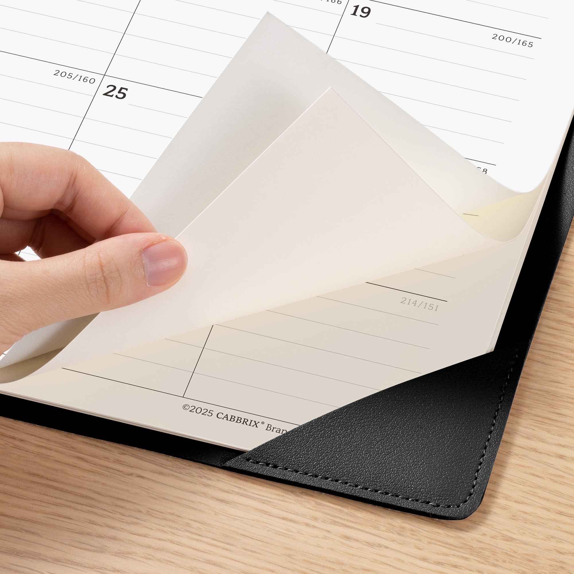 Hand holding a black notebook with lined pages on a wooden surface