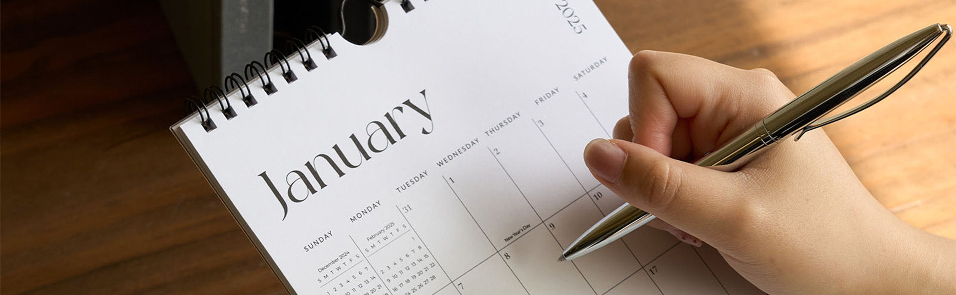 Hand holding a pen over a calendar with January 2023 on a wooden surface