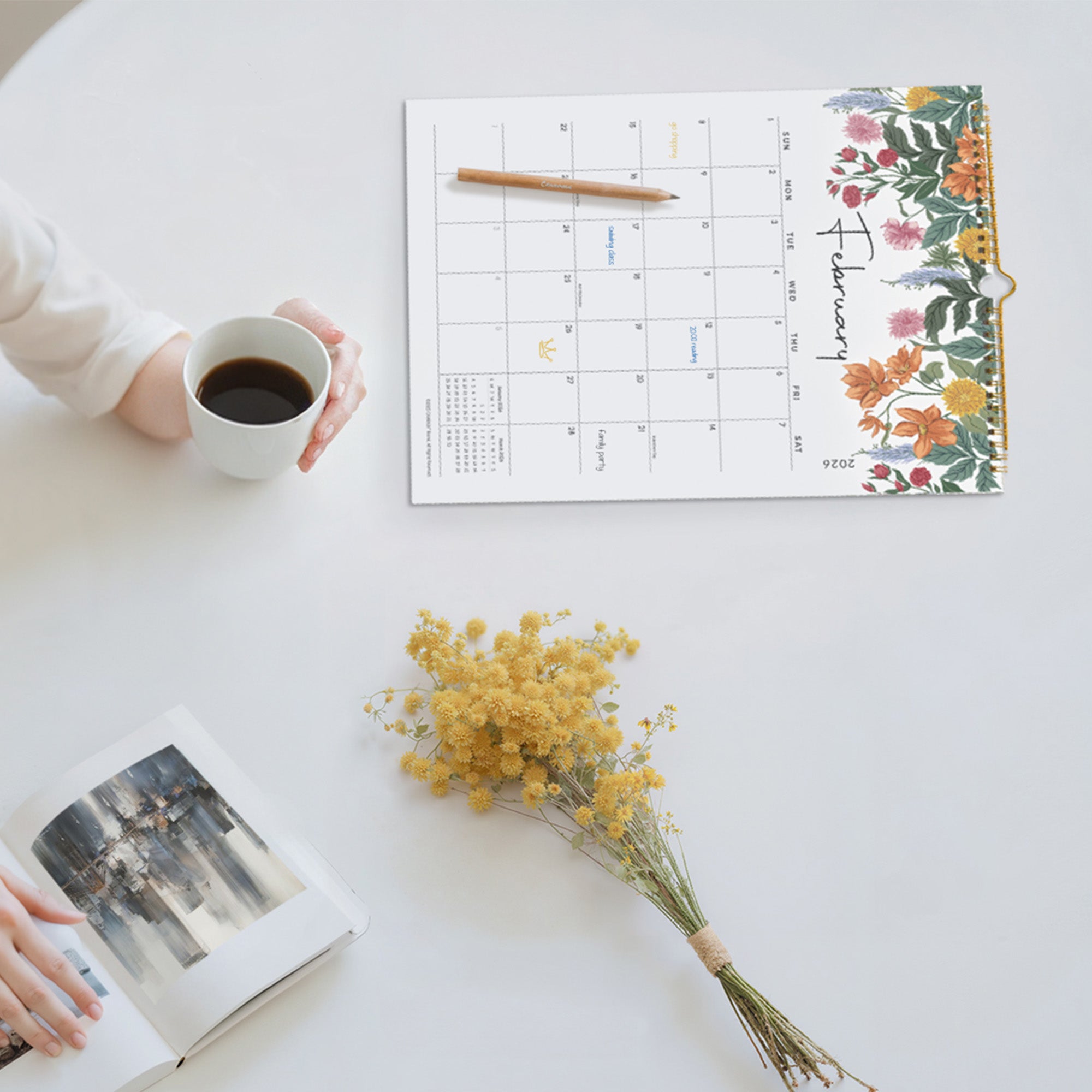 Person holding a cup of coffee with a calendar and book on a white surface