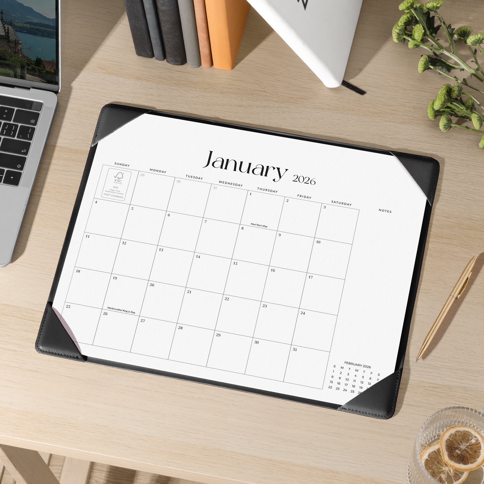 Calendar pad for January 2026 on a desk with a laptop and pen.
