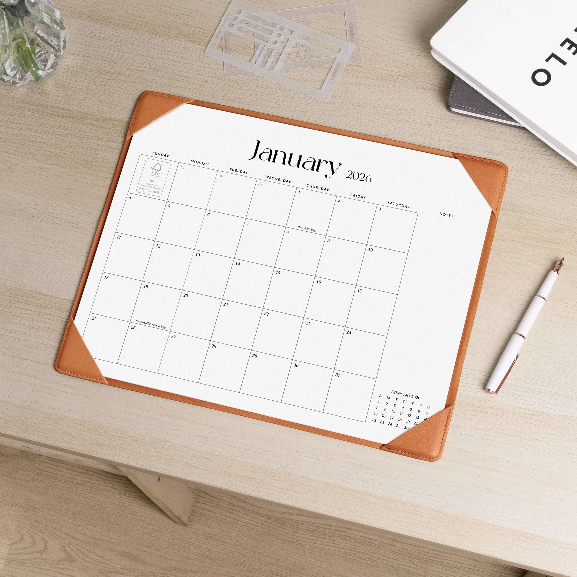 Calendar pad with January 2026 on a wooden desk with a pen and glass.