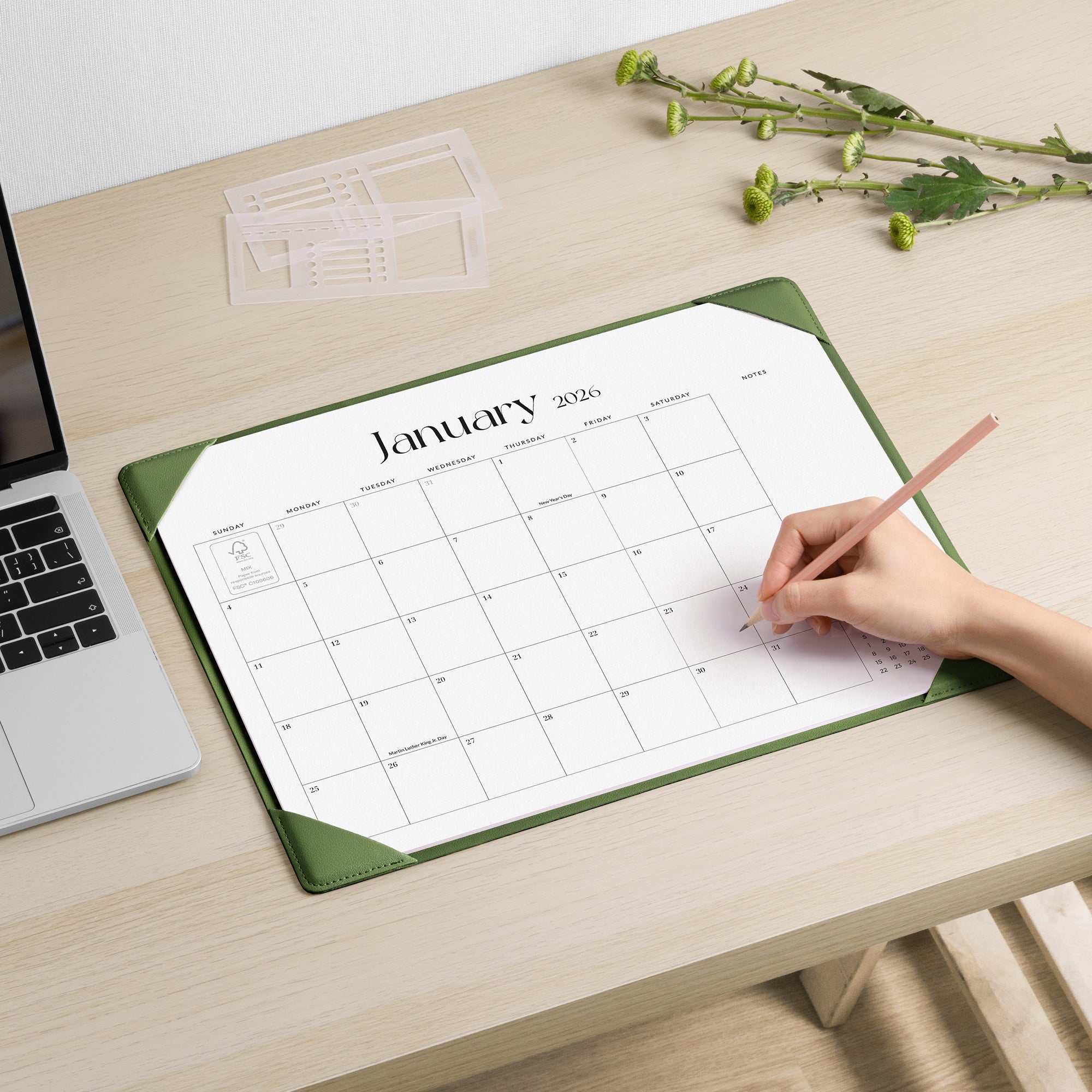 Person using a desk pad with a January 2020 calendar on a wooden desk.