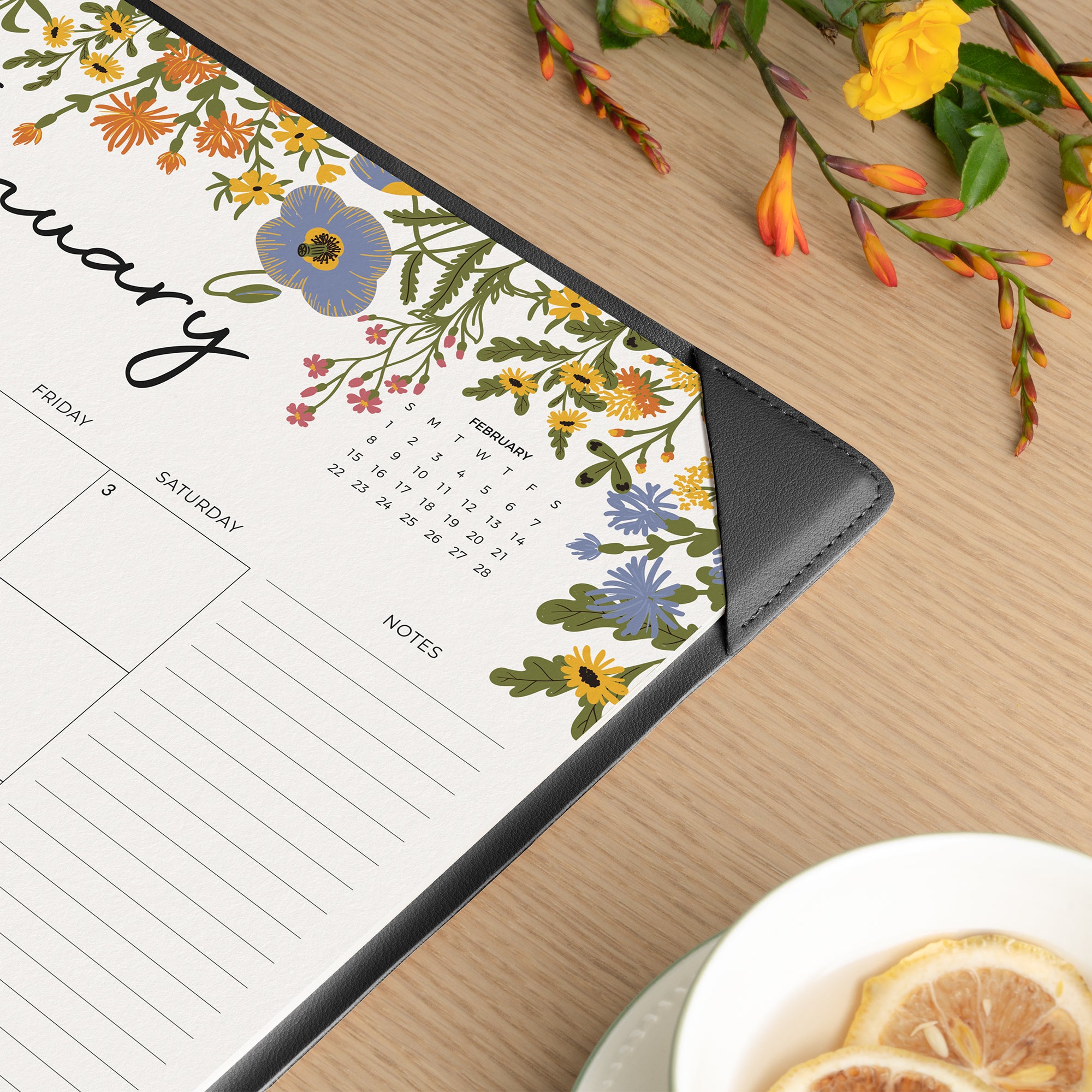 Floral-themed calendar on a wooden surface with a cup of tea and lemon slices.