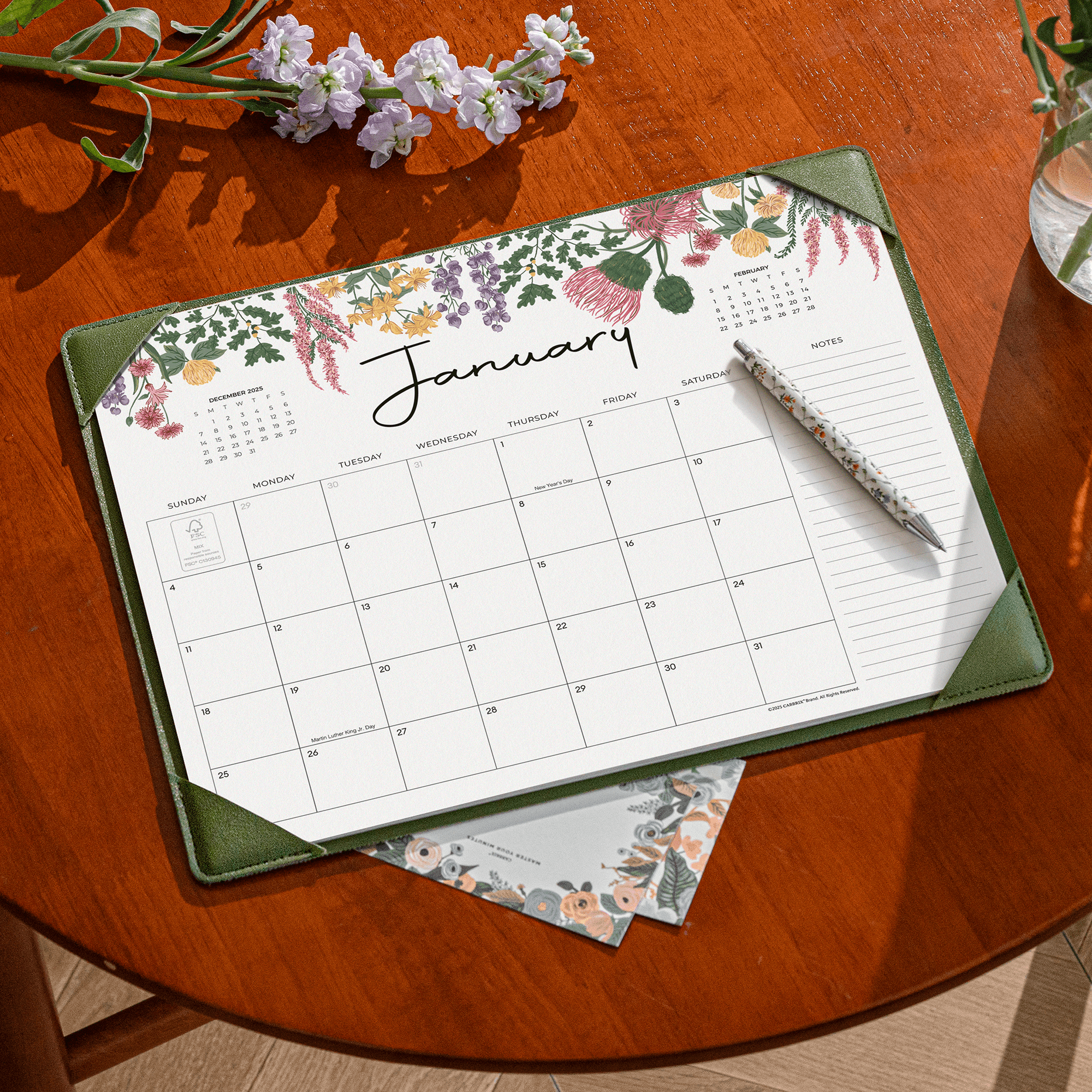 Floral calendar on a wooden table with a pen and small plant
