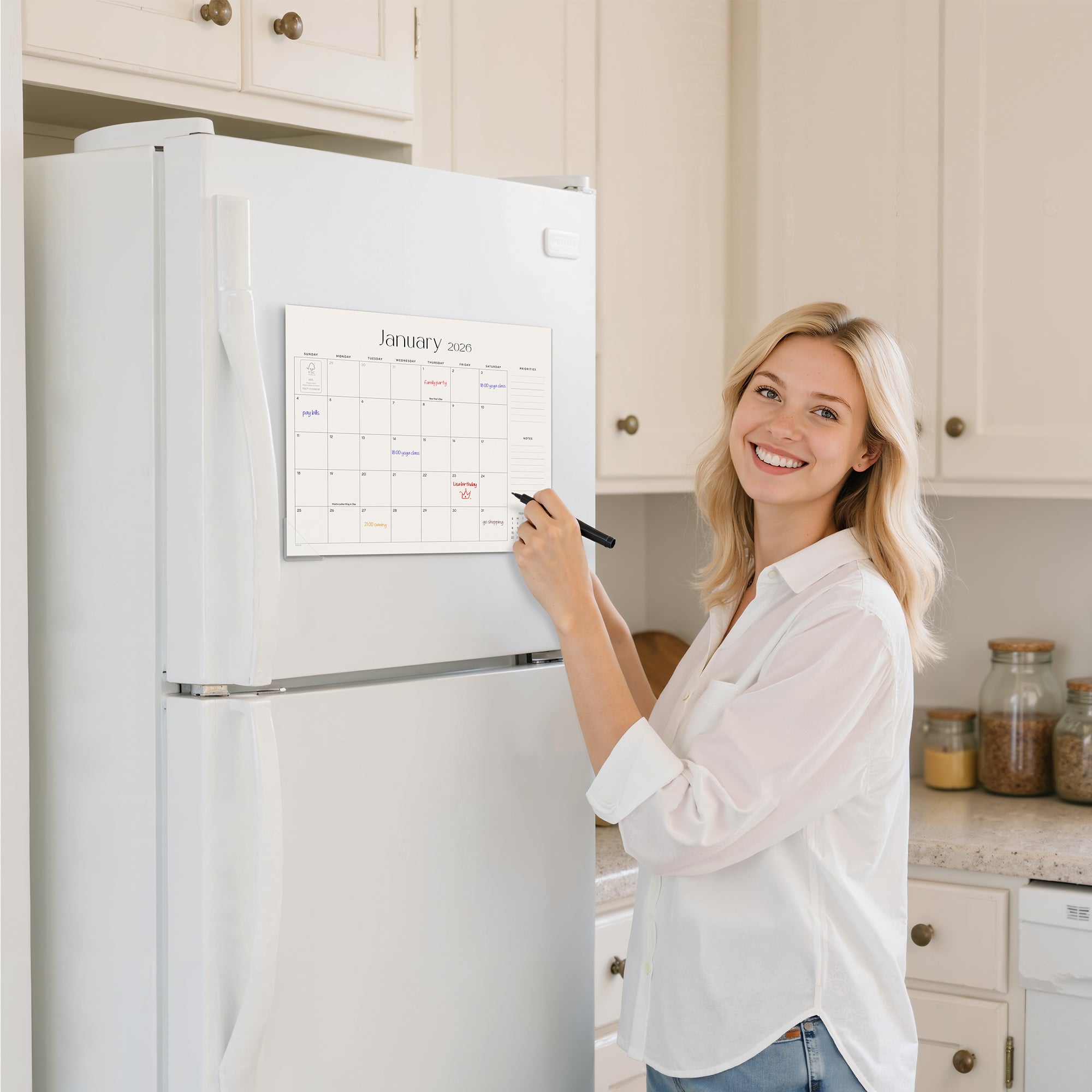 Woman writing on a calendar attached to a refrigerator in a kitchen.