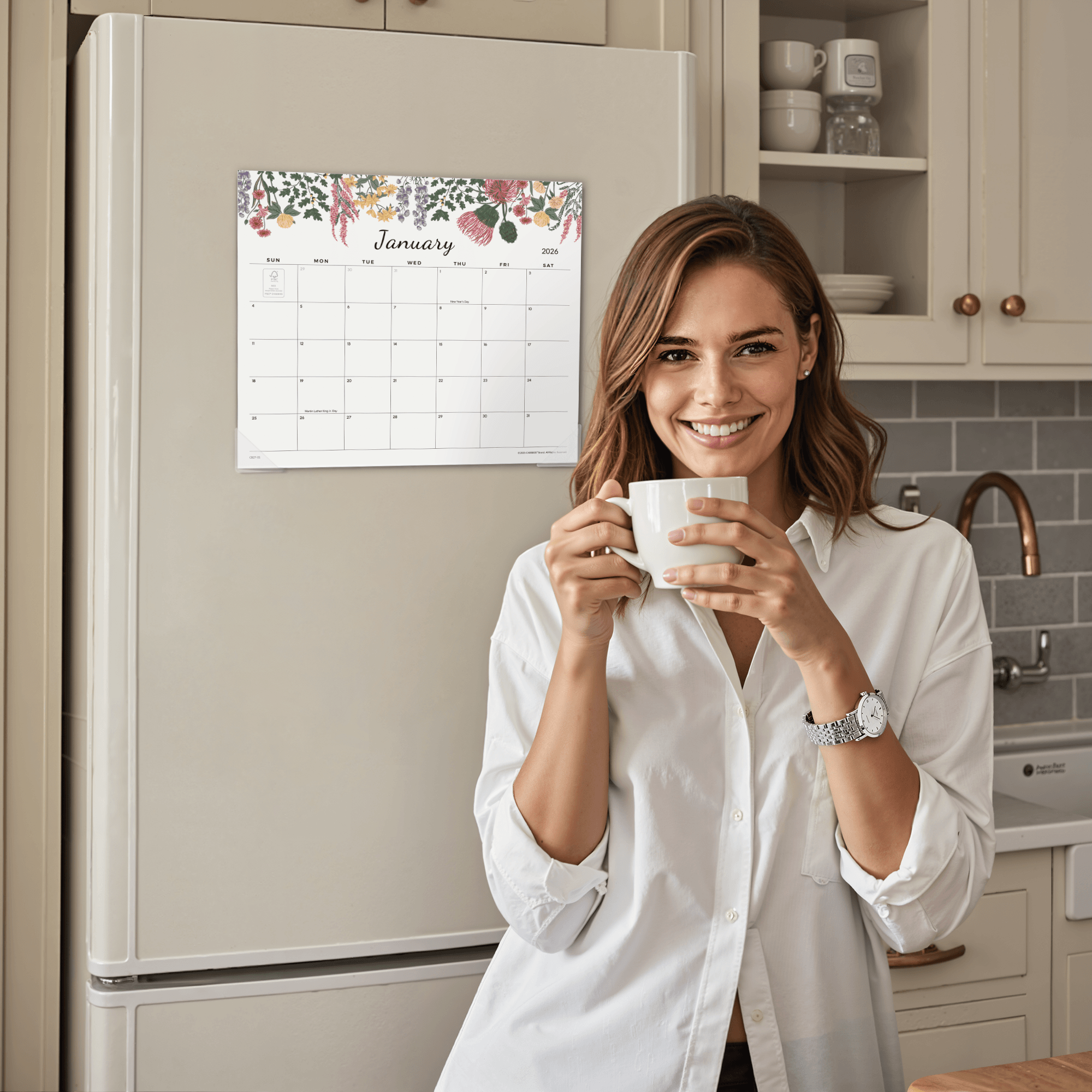 Woman holding a mug in a kitchen with a calendar on the refrigerator.