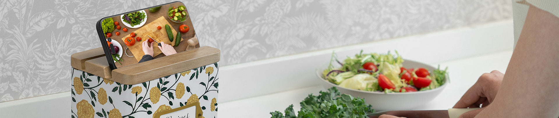 Person using a smartphone with a food app over a bread bin, next to a bowl of salad on a kitchen counter.