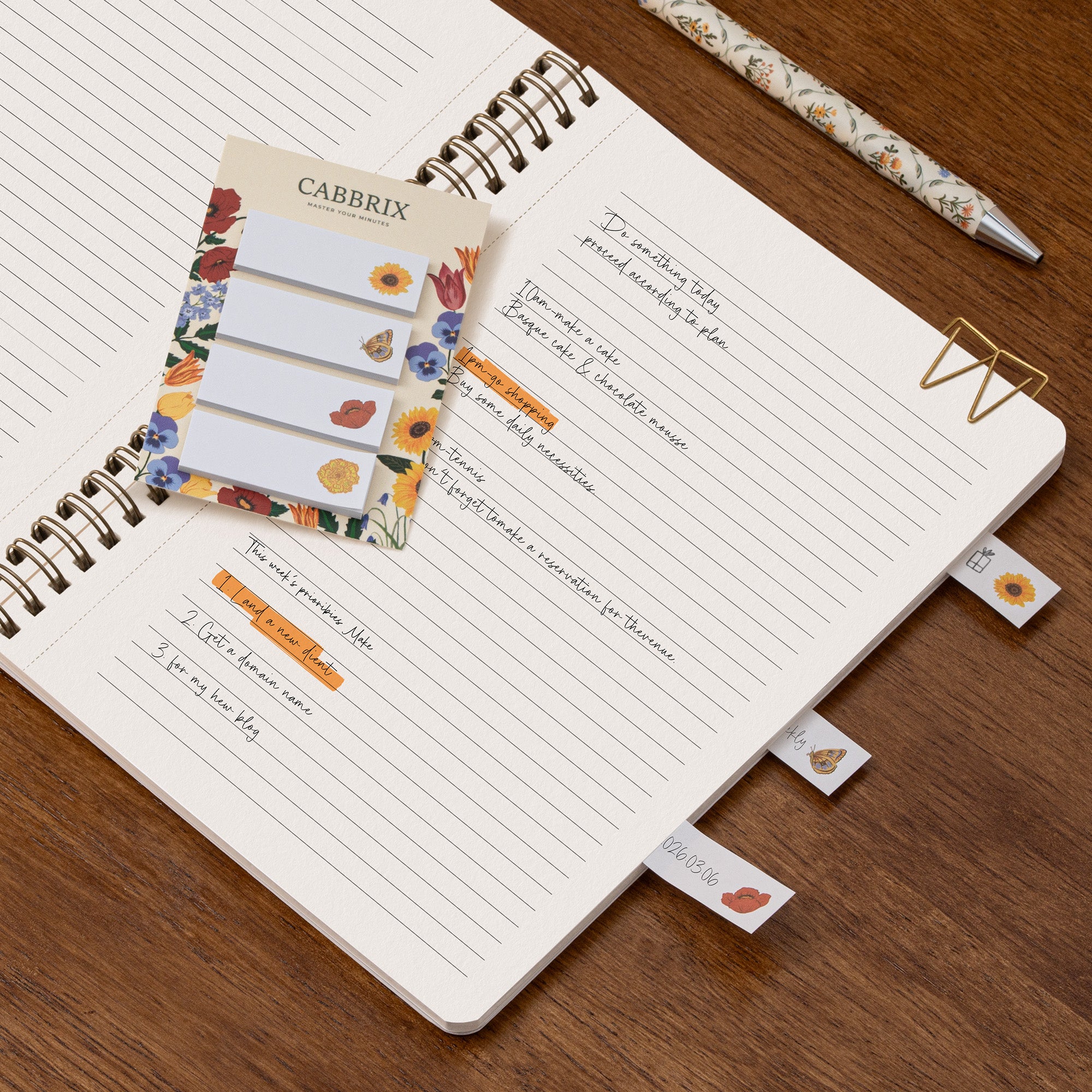 Notebook with floral sticky notes and decorative paper clips on a wooden surface
