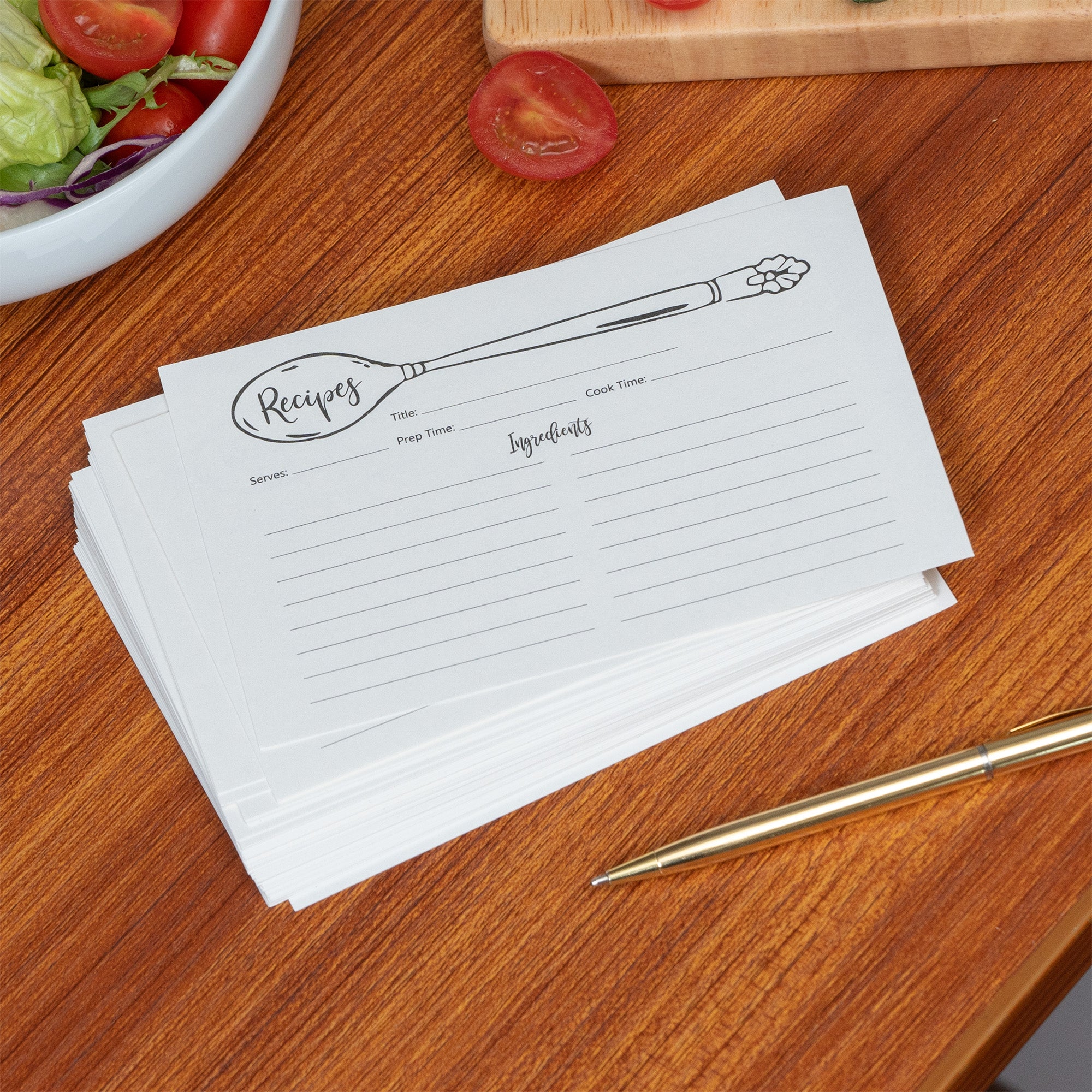 Stack of recipe cards on a wooden table with a pen and salad in the background