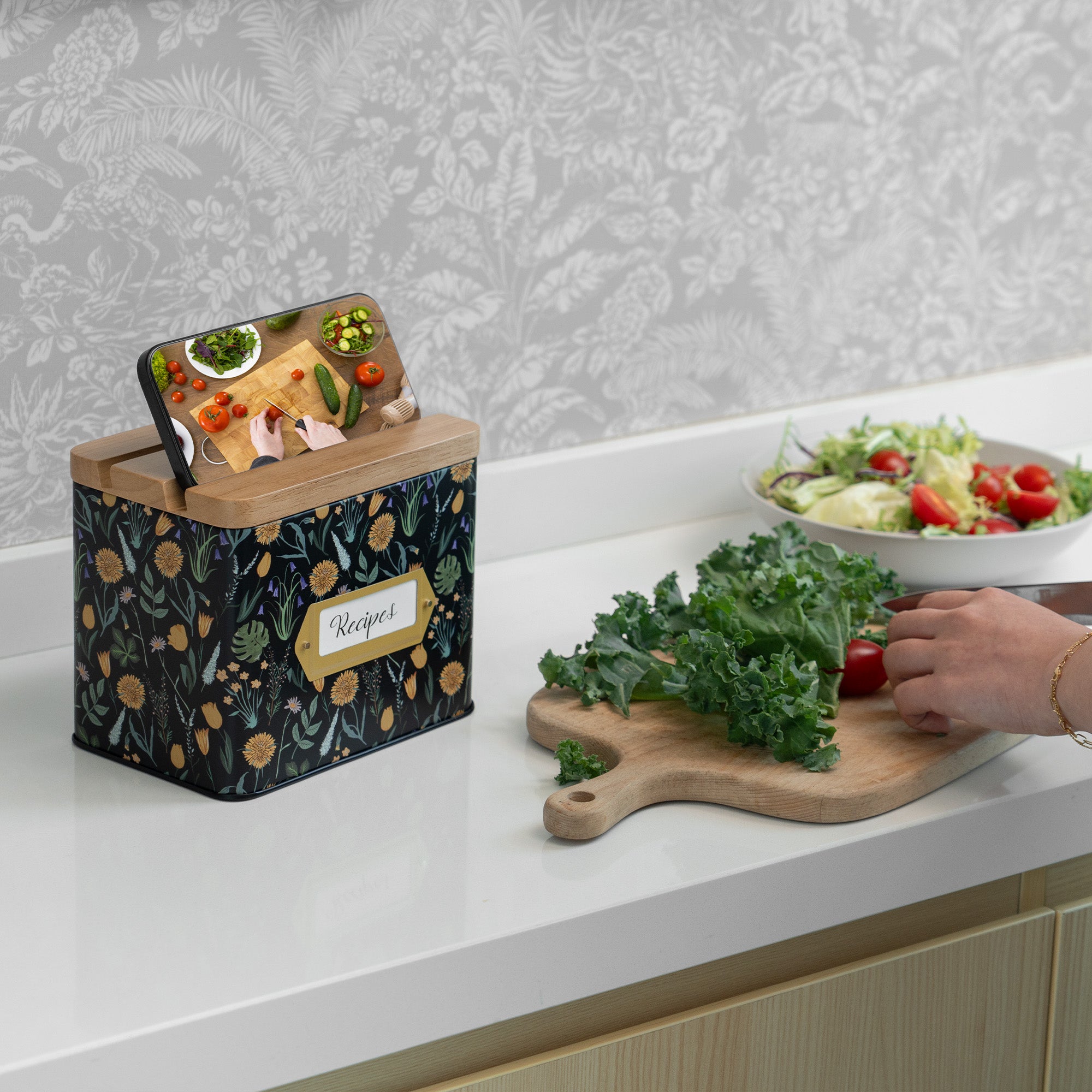 Kitchen counter with a recipe book, cutting board with greens, and salad bowl.