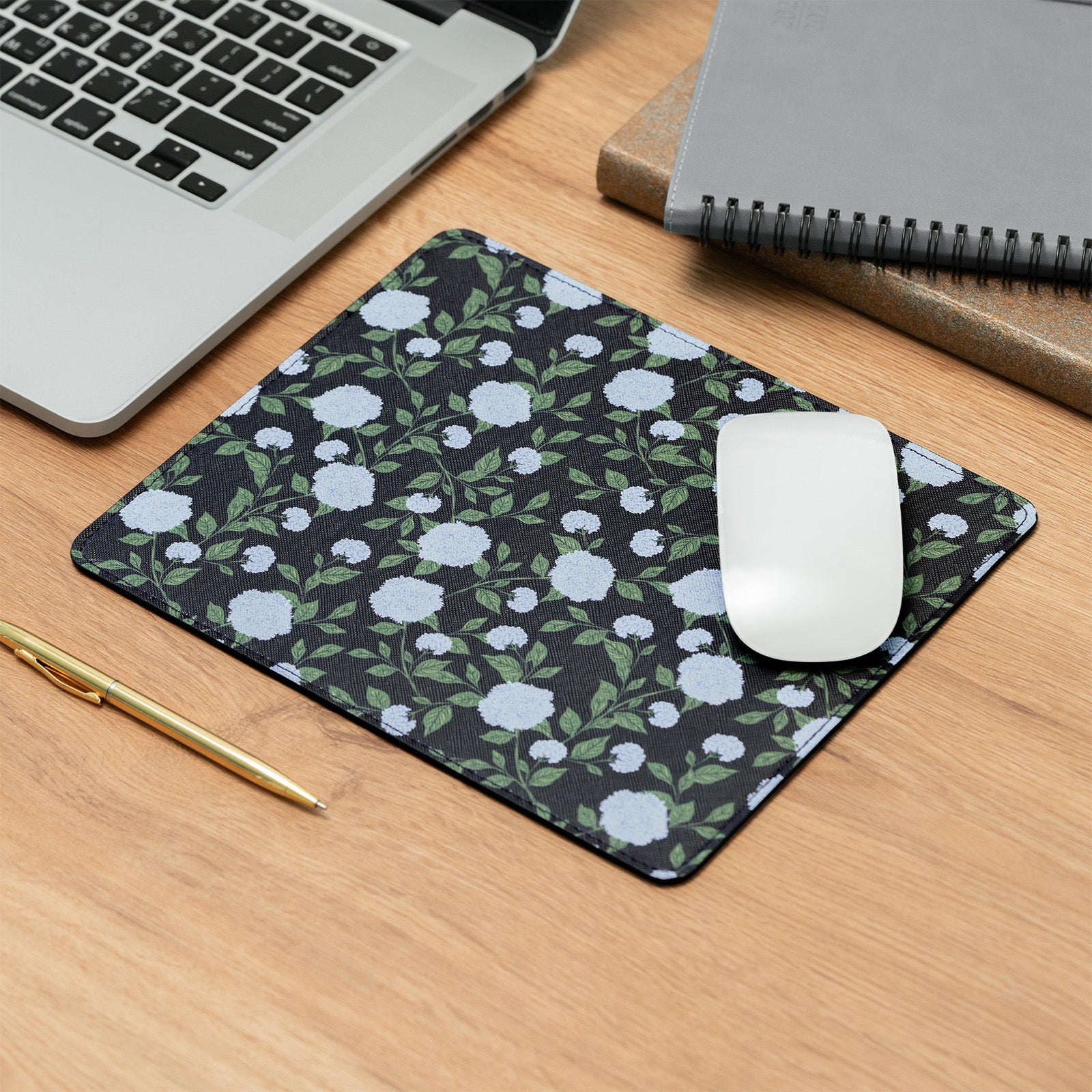 Floral mouse pad on a desk with a laptop, notebook, and pen.