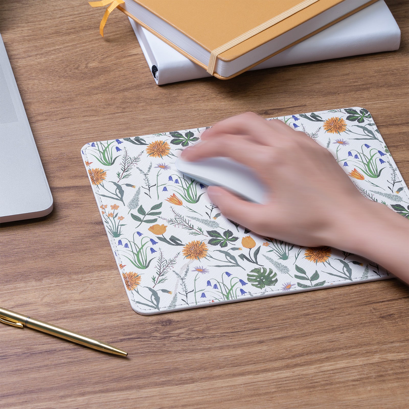 Hand using a mouse on a floral mouse pad with a notebook and pen in the background.