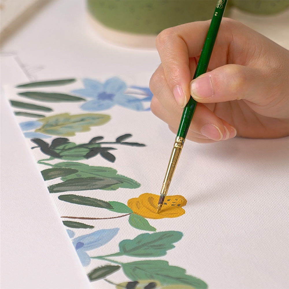 Hand painting a floral design on fabric with a green brush.