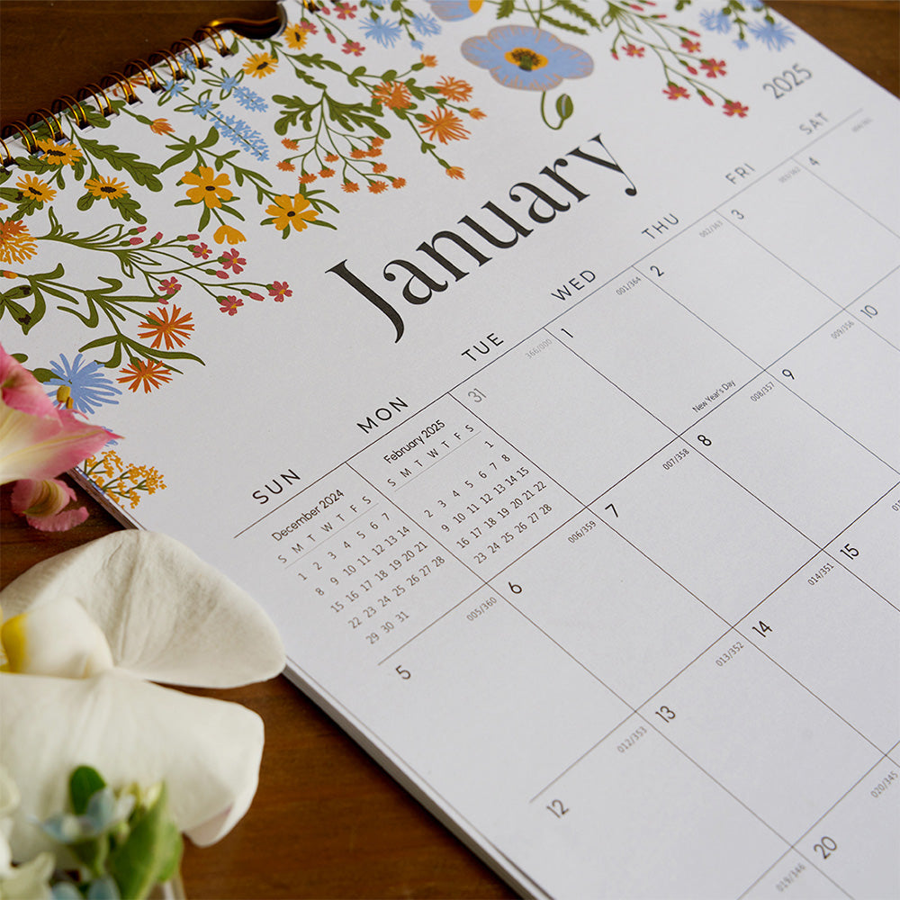 Calendar with floral design on the cover, open to January, on a wooden surface with flowers.