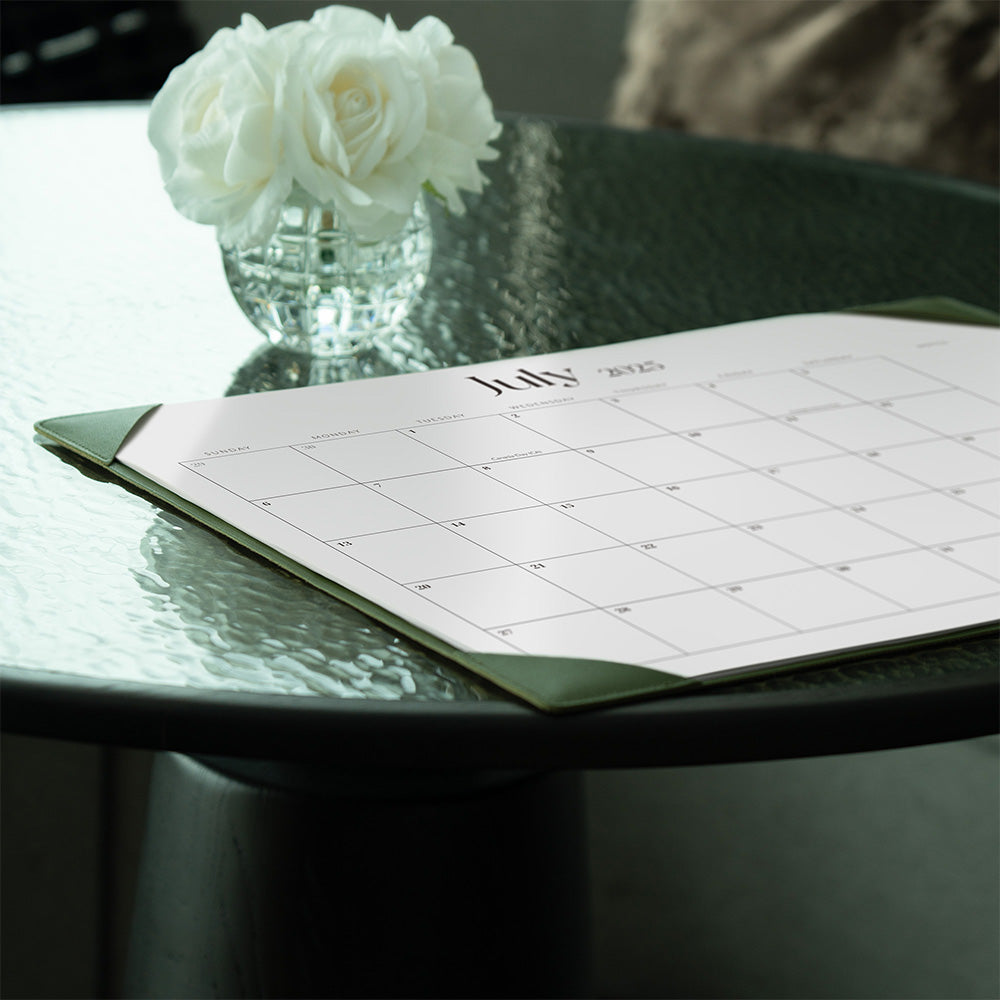 Calendar open to July on a glass table with white flowers in the background