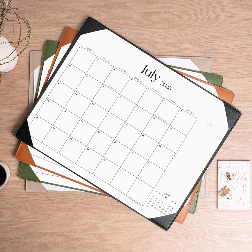 Calendar for July 2025 on a wooden surface with stationery items.