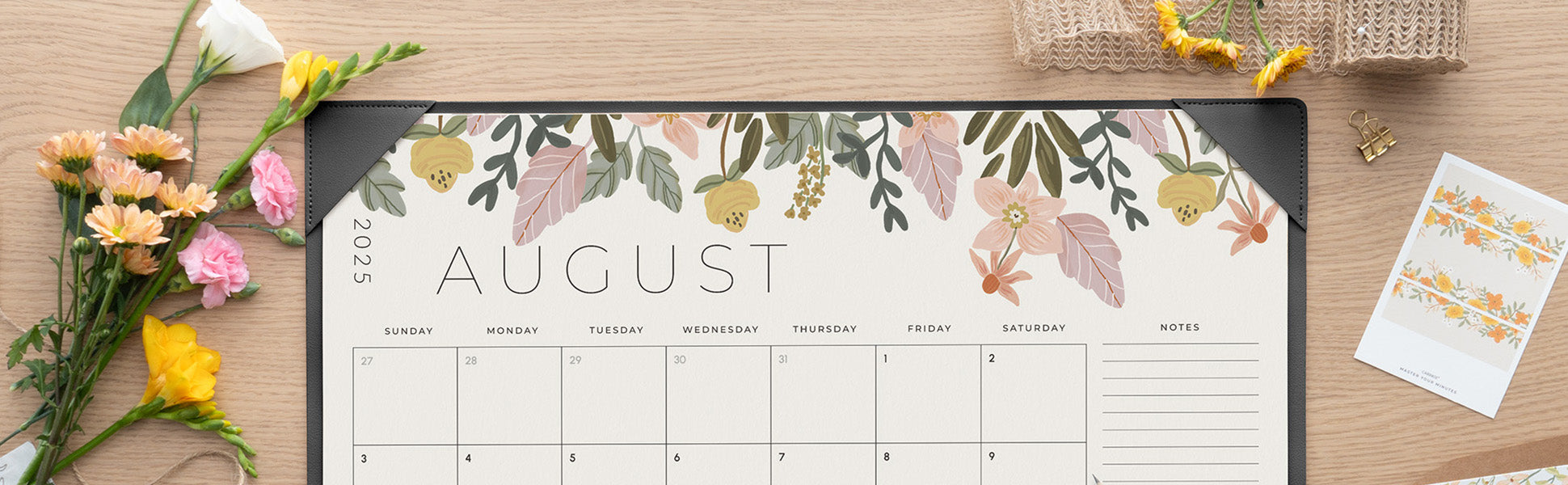 Floral-themed August calendar on a wooden surface with flowers and a basket.