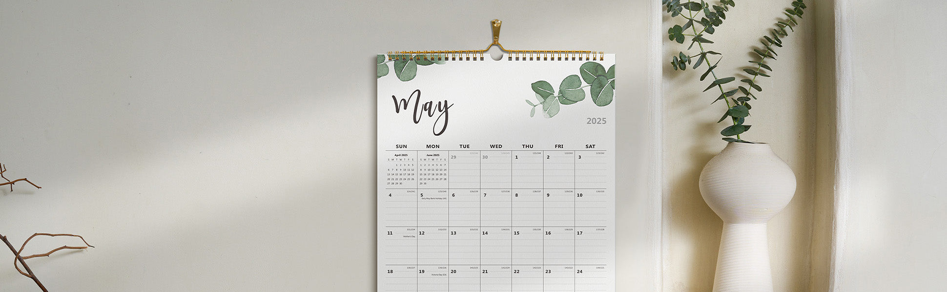 Calendar with May on a white wall next to a vase with greenery