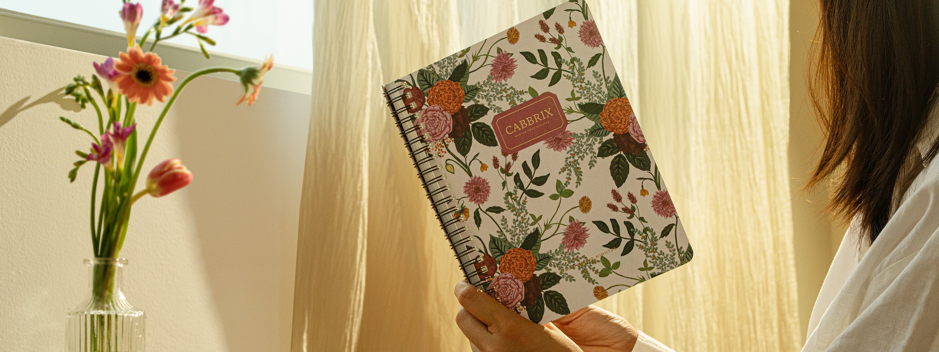 Person holding a floral notebook with a vase of flowers in the background