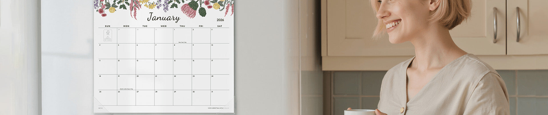 Woman in a kitchen holding a cup, with a calendar on the wall showing January.